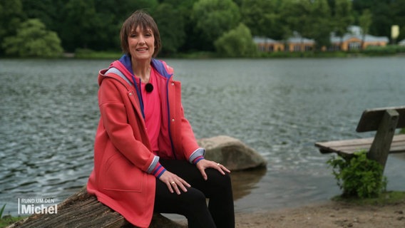 Theresa Pöhls moderiert die Sendung "Rund um den Michel" an einem See, der im Hintergrund zu sehen ist. © Screenshot 