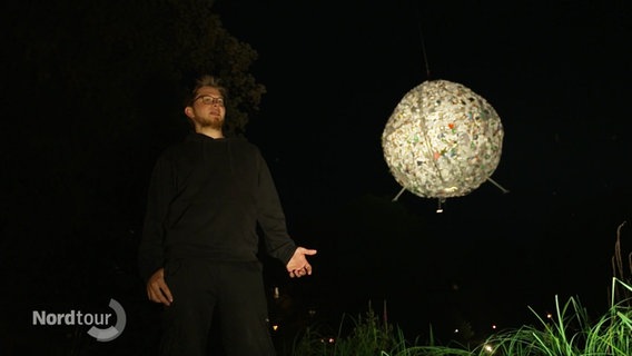 In der Dunkelheit erhebt sich ein beleuchteter Ball aus Plastikmüll, der an den Mond erinnert. © Screenshot 