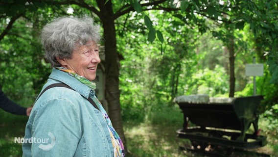 Brigitte Königstedt steht in einem Waldgebiet und weist die Relikte der ehemaligen Tongrube hin. © Screenshot 