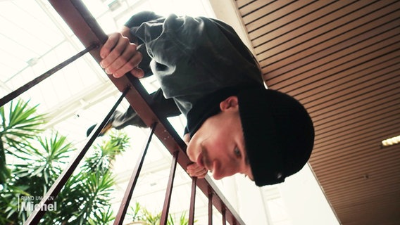 Ein junger Mann stützt sich kopfüber an einem Geländer ab. © Screenshot 