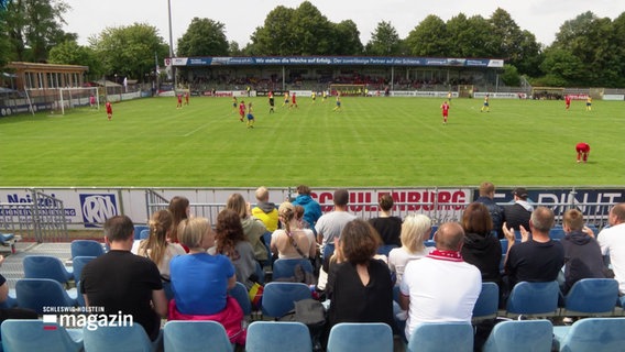 Blick über die Zuschauertribüne auf den Rasen, auf dem ein Fußballspiel stattfindet © Screenshot 