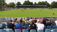 Blick über die Zuschauertribüne auf den Rasen, auf dem ein Fußballspiel stattfindet © Screenshot 