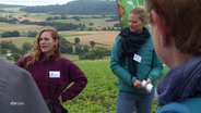 Zwei Frauen stehen in einem Ackergebiet und sprechen zu anderen Personen. © Screenshot 