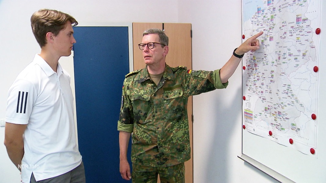 Ein Mann in Uniform zeigt einem Schüler etwas auf einer Karte.