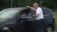 Ein Mann steht neben einem Auto und spricht mit dem Fahrer. © Screenshot 