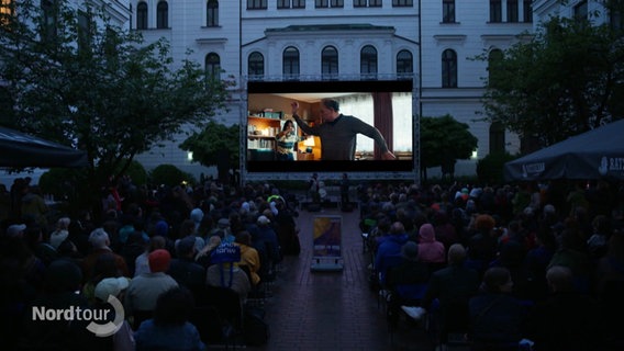 Kinopublikum im Innenhof des Altonaer Rathauses schaut unter freiem Himmel einen Film auf großer Leinwand. © Screenshot 