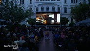 Kinopublikum im Innenhof des Altonaer Rathauses schaut unter freiem Himmel einen Film auf großer Leinwand. © Screenshot 