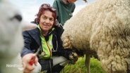 Eine Frau hockt neben einem Schaf auf einer Wiese und behandelt es. © Screenshot 