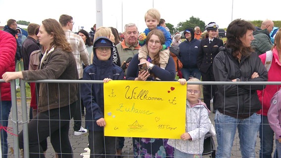 Angehörige halten ein Schild mit der Aufschrift: "Wilkommen zuhause". © Screenshot 