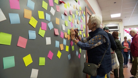 Eine Besucherin im NDR Pop-Up-Studio in Harburg schreibt auf einer Wand mit vielen bunten Zetteln. © Screenshot 