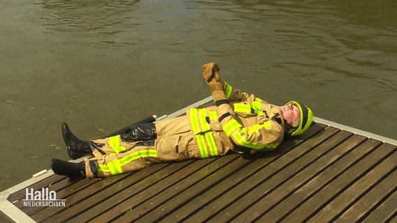 Ein Mann in Feuerwehrkleidung liegt erschöpft auf einem Steg an der Weser © Screenshot 