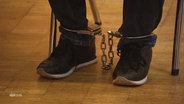 Der Angeklagte trägt Fußfesseln. © Screenshot 