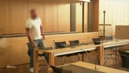 Ein Mann steht in einem Gerichtssaal. Er trägt ein weißes T-Shirt und eine blaue Jeans, sein Gesicht ist unkenntlich gemacht. © Screenshot 