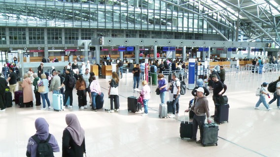 Eine Gruppe von Menschen mit Urlaubsgepäck steht am Hamburger Flughafen in einer Schlange. © Screenshot 