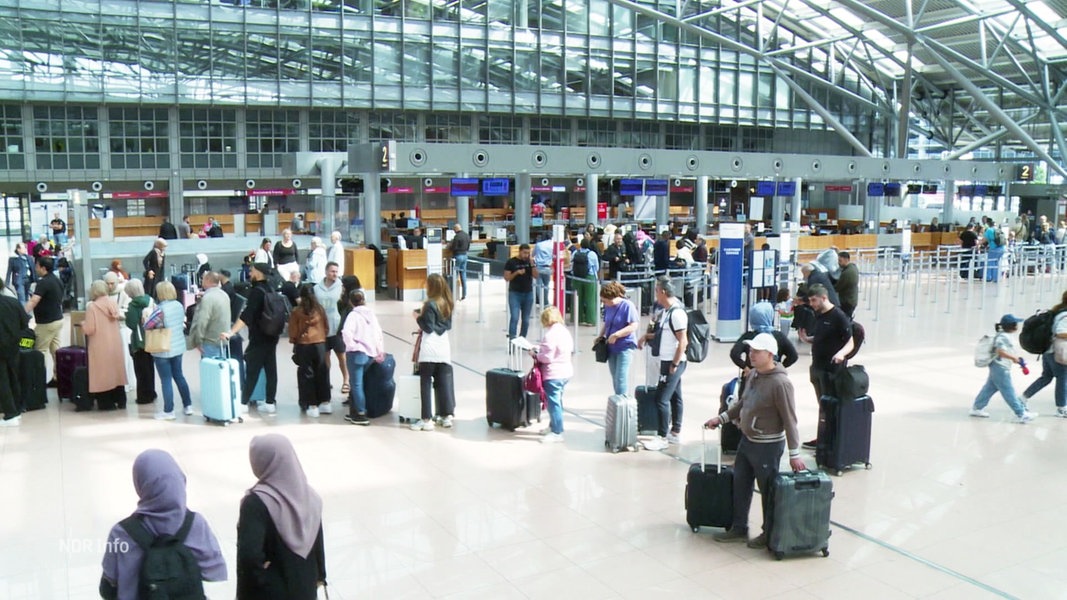 Eine Gruppe von Menschen mit Urlaubsgepäck steht am Hamburger Flughafen in einer Schlange.