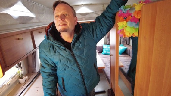 Campingfan Friso Richter steht in einem Wohnmobil. Links und rechts von ihm sind Arbeitsflächen und Schränke. Hinter ihm ist eine Sitzecke mit Tisch zu erkennen. © Screenshot 