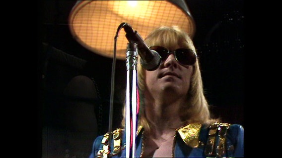 Frontsänger der Band The Sweet Brian Connoly. Er trägt blonde kinnlange Haare mit einem Pony und eine Sonnebrille. (Aufnahme aus der Sendung "Musikladen" vom 13. November 1974. © Screenshot 