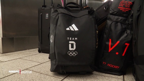 Eine schwarze Reisetasche mit weißen Olympia-Logo steht gepackt auf dem Boden. © Screenshot 