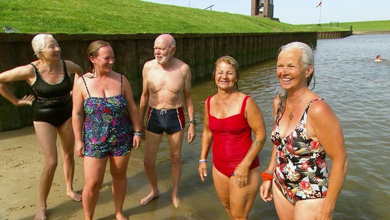 Fünf Menschen im Seniorenalter stehen gut gelaunt in Badekleidung vor dem Gewässer des Jadebusens, in dem sie kurz zuvor schwimmen waren. © Screenshot 