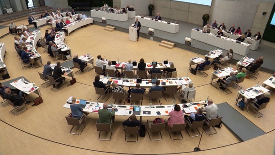 Der Kreistag von Ludwigslust-Parchim von oben fotografiert. In einem Halbkreis sitzen die Abgeordneten an weißen Tischen um das zentral aufgestellte Rednerpult, vor sich auf den Tischen liegen Unterlagen. © Screenshot Foto: NDR