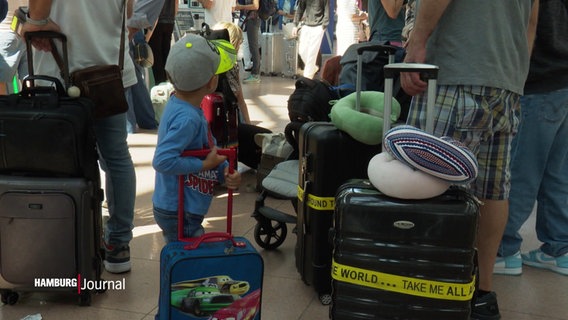 Szene am Flughafen Hamburg: Ein Kind inmitten von Koffern. Es hält einen Kinder-Koffer fest. © Screenshot 