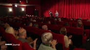 Im Kinosaal mit applaudierendem Publikum und Filmmacher:innen. © Screenshot 