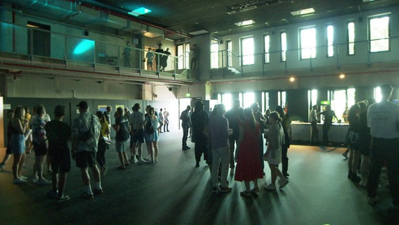 Menschen stehen im Gegenlicht in der neuen Veranstaltungshalle im Grünen Bunker in Hamburg-St. Pauli. © Screenshot 