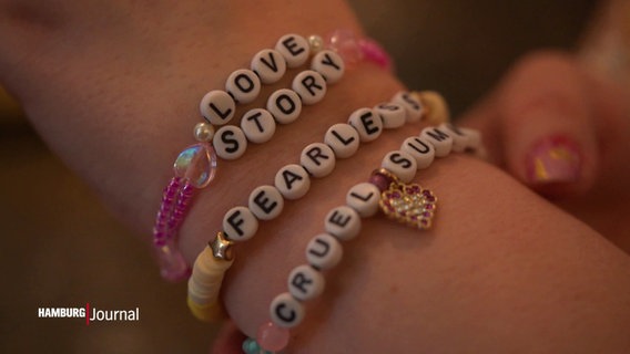 Na jednym nadgarstku zawiązuje się domowe bransoletki z koralików z literami przedstawiającymi tytuły piosenek Taylor Swift.  © Zrzut ekranu 