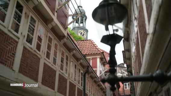 Hinter einer schmalen Gasse mit Fachwerkhäusern sieht man den Turm des Hamburger Michels. © Screenshot 