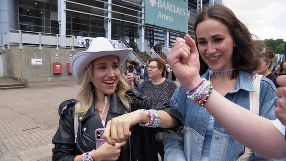 Junge Frauen zeigen sich gegenseitig ihre Taylor-Swift-Armbänder. © Screenshot 