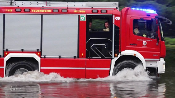 Ein Feuerwehrauto fährt über eine überschwemmte Straße. © Screenshot 