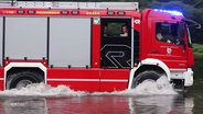 Ein Feuerwehrauto fährt über eine überschwemmte Straße. © Screenshot 