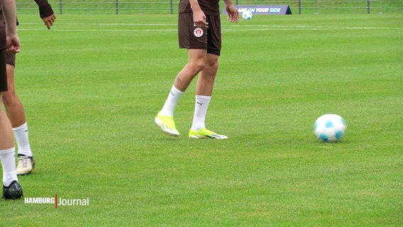 Auf einem Rasenplatz sieht man ein paar Fußballer-Beine in braunen Trainingshosen. © Screenshot 