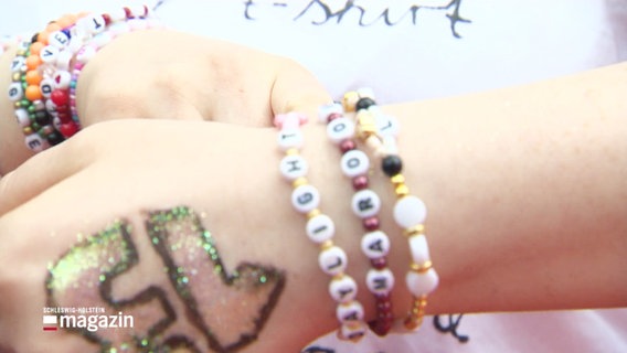 Perlenarmbänder mit Songtiteln von Taylor Swift hängen einem Handgelenk. © Screenshot 