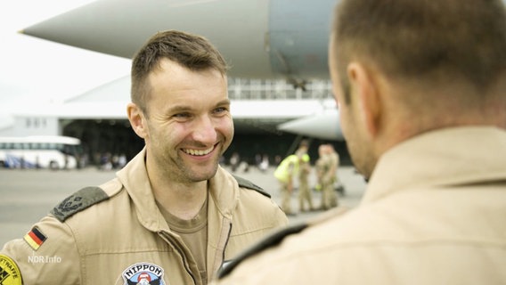 Kampfpilot Marco Brunhofer lächelt einem Kollegen zu, im Hintergrund ein Eurofighter. © Screenshot 
