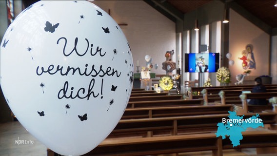 In einer Kirche stehen Blumen und Fotos zum dedenken an einen toten Jungen, im Vordergrund sieht man einen Ballon mit der Aufschrift: "Wir vermissen dich!". © Screenshot 