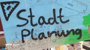 Schild mit aufgesprühtem Schriftzug: "Stadtplanung". © Screenshot 