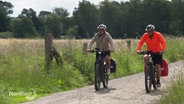 Zwei Männer fahren auf Rädern an einem Feld vorbei. © NDR 