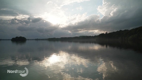 Sonne und Wolken spiegeln sich auf einem See. © Screenshot 
