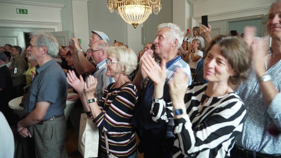 Menschen applaudieren beim Public Viewing zur Vergabe des Weltkulturerbe-Titels im Demmlersaal in Schwerin © Screenshot 