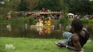Eine Person liegt mit Blick aufs Reggae Jam Festival an einem See. © Screenshot 