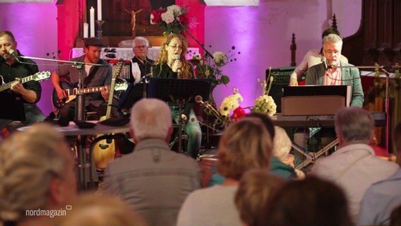 Eine Pastorin singt beim Rockgottesdienst in Zemmin, um sie herum Musiker und Besucher:innen. © Screenshot 