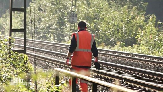 Ein Mann in orange-farbener Sicherheitskleidung läuft an Bahngleisen entlang. © Screenshot 