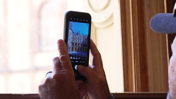 Ein Mann fotografiert das Schweriner Residenzensemble mit seiner Handy-Kamera. © Screenshot 