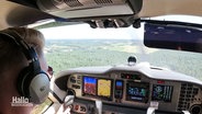 Ein Pilot sitzt im Cockpit eines kleinen Flugzeugs und blickt auf die Landschaft. © Screenshot 