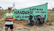 Radler Andreas Beneke posiert vor einem Schild mit der Aufschrift "Hanover Welcome". © Screenshot 