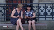 Zwei Personen sitzen nebeneinander und schauen auf ein Smartphone. © Screenshot 