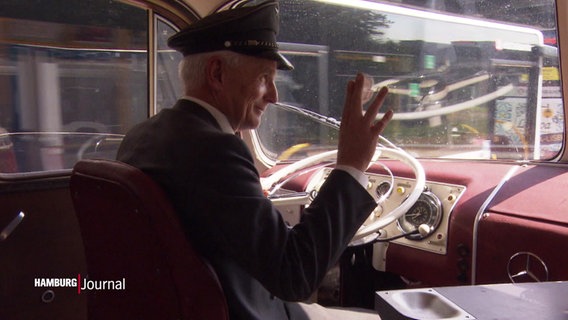 Der Fahrer eines historischen Omnibusses grüßt vom Fahrersitz und lächelt freudig. © Screenshot 