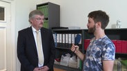 NDR Reporter Jürn-Jacob Gericke spricht mit Fabian Rüsch, Fachanwalt für Verkehrsrecht. Im Hintergrund ist ein Regal mit Ordnern vor einer weißen Wand zu sehen. © Screenshot 