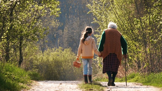 Ein junges Mädchen und eine alte Frau gehen auf einem Weg Hand in Hand. © Screenshot 